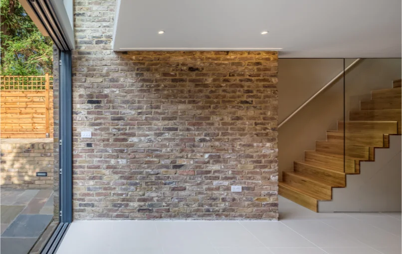 This image depicts a stone wall that supports the house. On the right is a staircase leading to the upper floor.