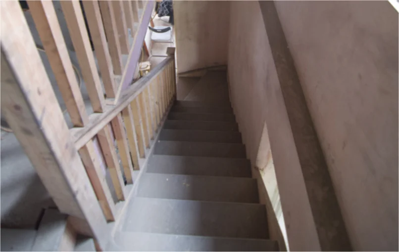 This image depicts a stairwell which has been plastered and a was given a new wooden hand rail.