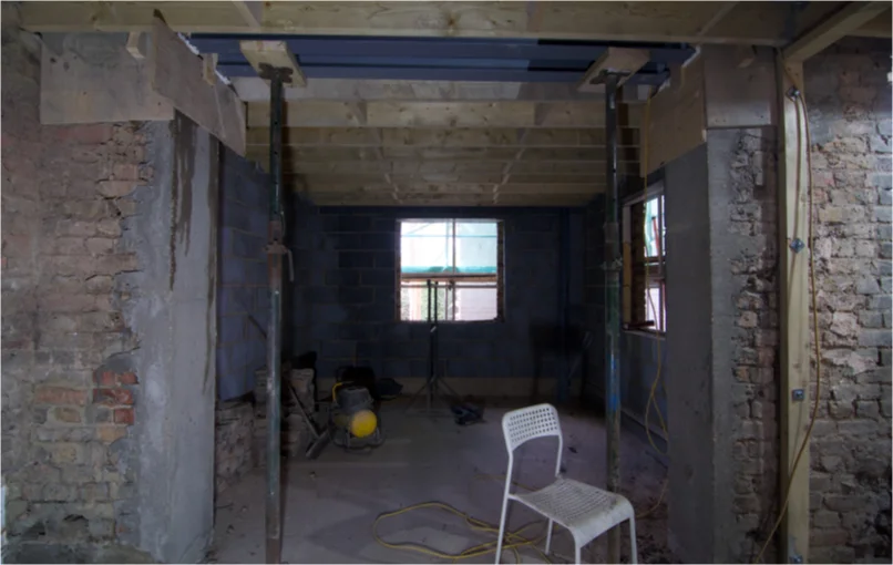 This image depicts a room with no plasterboard or windows put in exposing the original brick work of the building mixed in with some new cinder blocks.